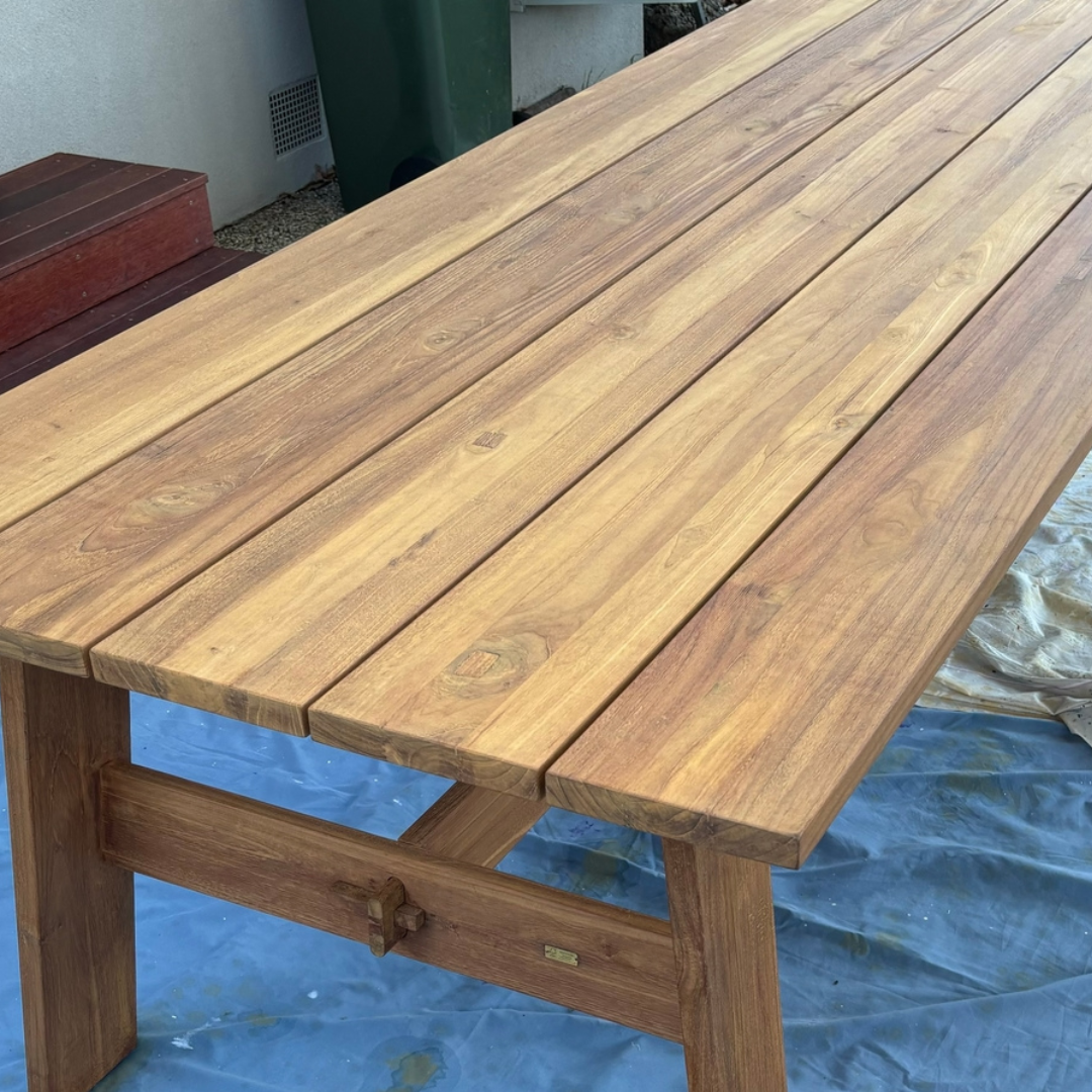 Wooden table with a blue tarp in the background, which has a new coat of Semco Natural Teak Sealer for protection