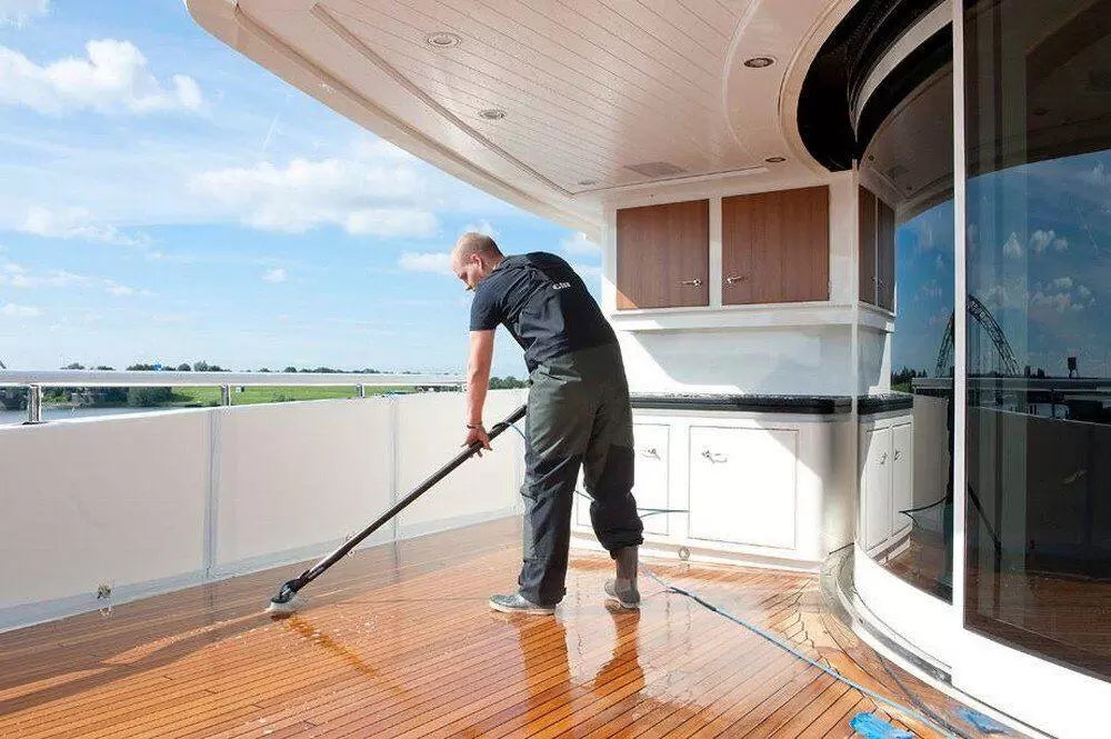 Person cleaning a wooden deck on a yacht with a blue sky and water in the background