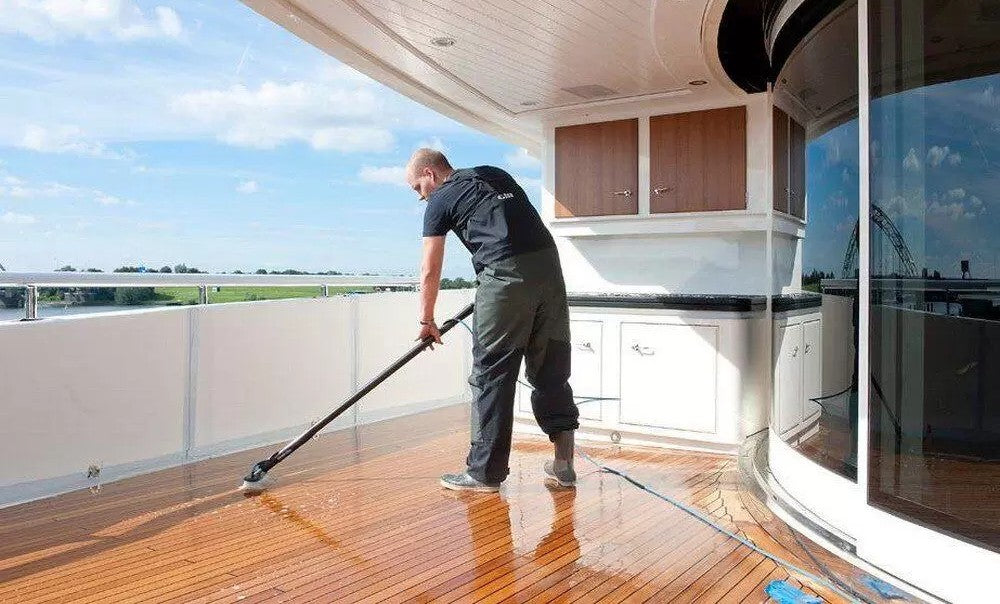 Person cleaning a wooden deck on a boat with a brush.